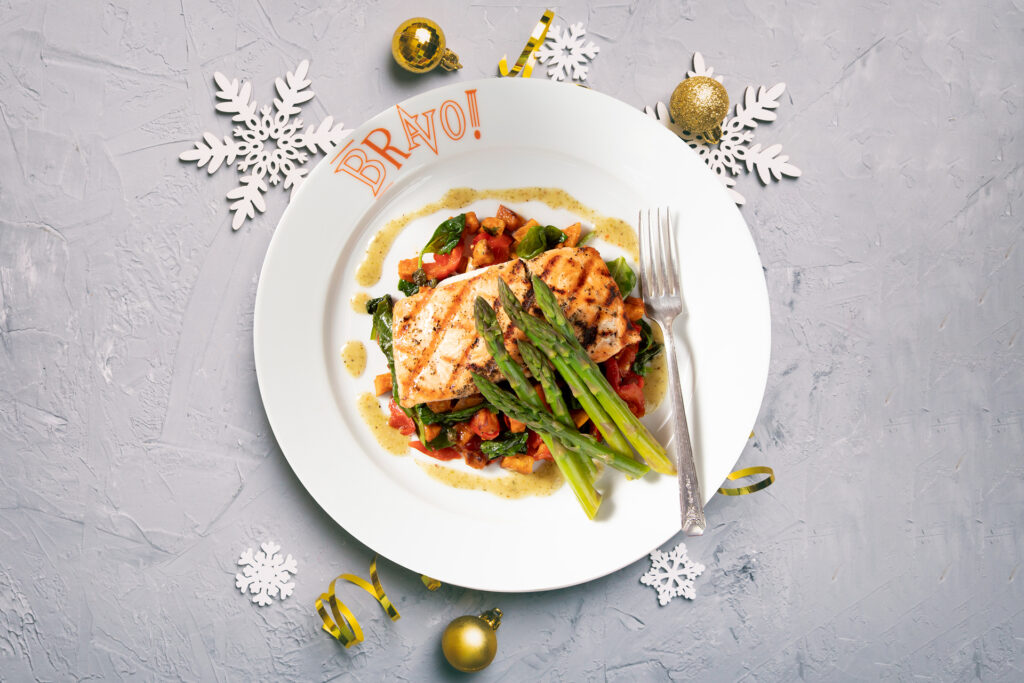 Grilled salmon served over a bed of sautéed spinach, diced tomatoes, and roasted vegetables, topped with fresh asparagus and drizzled with a light herb sauce, presented on a festive plate from Bravo Italian Kitchen.