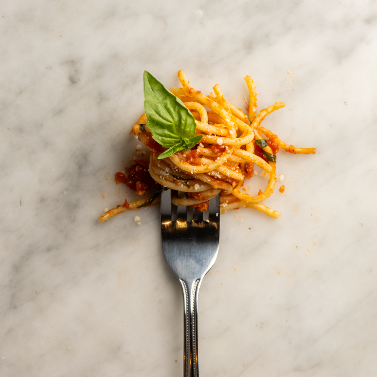 A fork with spaghetti neartly curled around the tines, garnished with basil