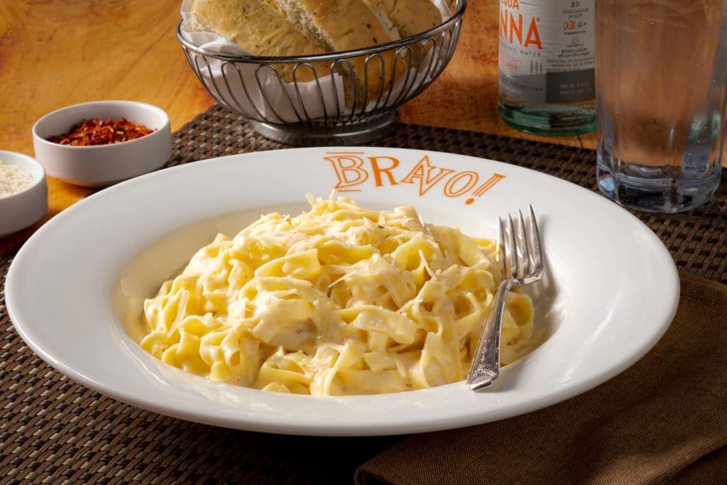 Bravo Fettucine Alfredo with beverage, bread, chili flakes, parmesan in the background